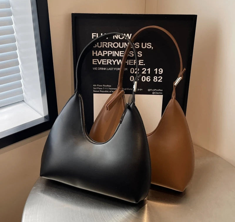 Two handbags, one black and one brown, on a reflective surface with a framed quote in the background.
